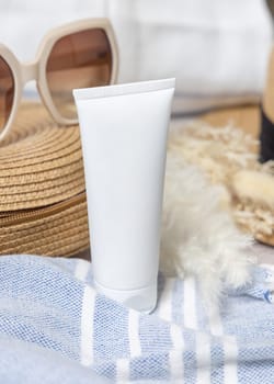 White blank squeeze cream tube on rattan bag near towel, dryed grass and sunglasses closeup. Sunscreen cosmetics mockup. Summer vacation with spf uv-protected sunbathing
