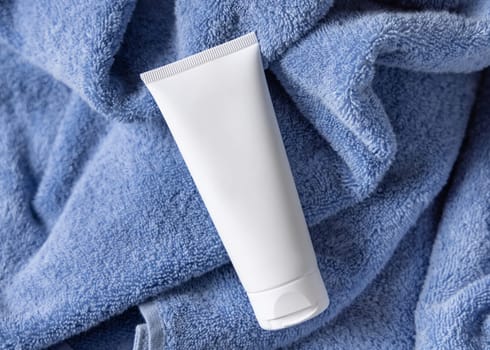 White blank squeeze cream tube on blue towel in bathroom top view, brand packaging mockup. Natural handmade cosmetic product for daily face or handcare, copy space