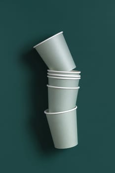 Disposable light green paper cups on a dark green background top view, mockup with advertising copy space. Empty cardboard coffee cups flat lay. No plastic and sustainable lifestyle concept
