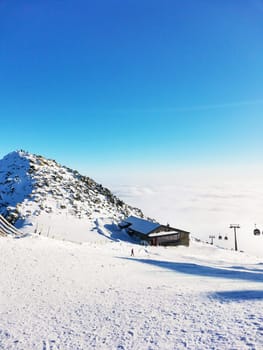 Ski resort. Mountain peak in the clouds. Wooden house on the background of mountains. Cable car. Clear sunny winter day