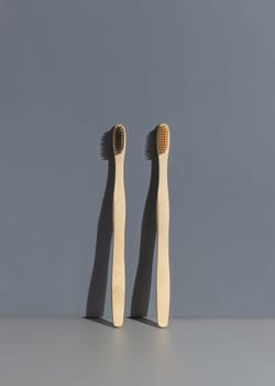 Two beige biodegradable bamboo toothbrushes on a grey background with hard shadow closeup, mockup, negative space. Natural personal accessories for dental care, minimal style aesthetic