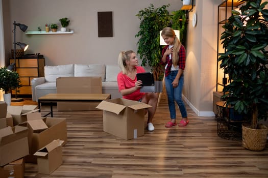 Two friends happily unpack in a cozy living room filled with boxes and lush greenery from various plants