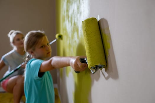 A young girl paints a wall with a roller while another child helps, showcasing teamwork and creativity.