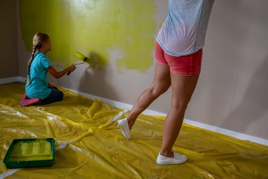 Two children joyfully painting a wall with vibrant yellow paint, showcasing teamwork and creativity.