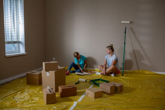 Two close friends actively engaged in a room renovation project, preparing to paint with supplies strewn around them