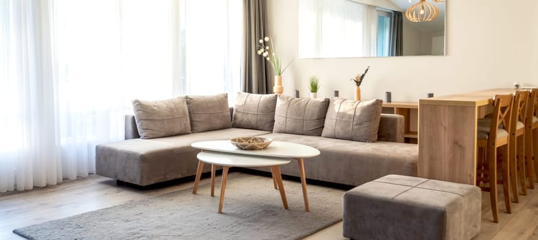 Modern living room with gray sectional sofa, white coffee table, wooden dining area, and natural light