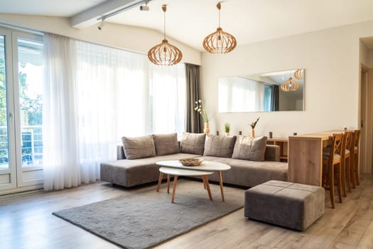 Bright modern living room with gray sectional sofa, white coffee table, wooden dining set, and large windows