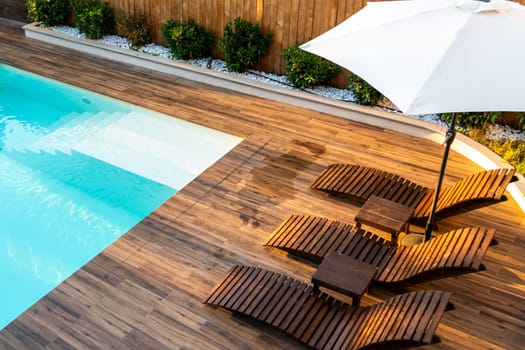 Luxury poolside wooden deck with modern lounge chairs, umbrella, and turquoise swimming pool