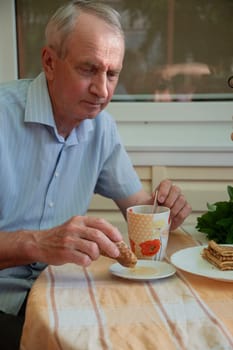 elderly man enjoying tea with pancakes, dipping rolled pancake in honey, late sweet breakfast,