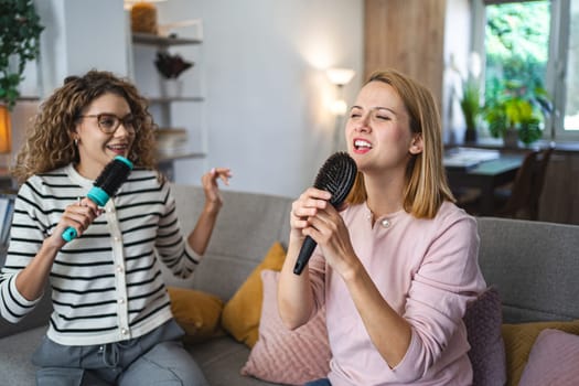 Two friends are sitting on the couch and having a great time singing into hairbrushes instead of microphones.