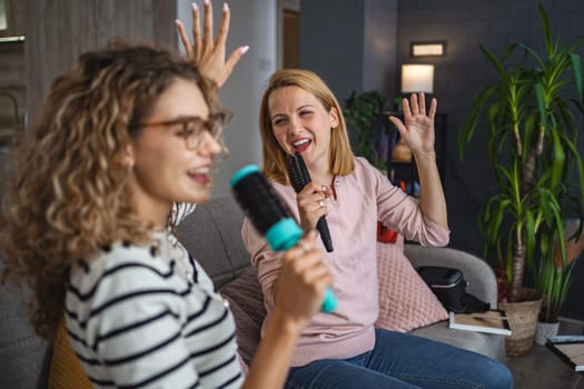 Two friends are sitting on the couch and having a great time singing into hairbrushes instead of microphones.