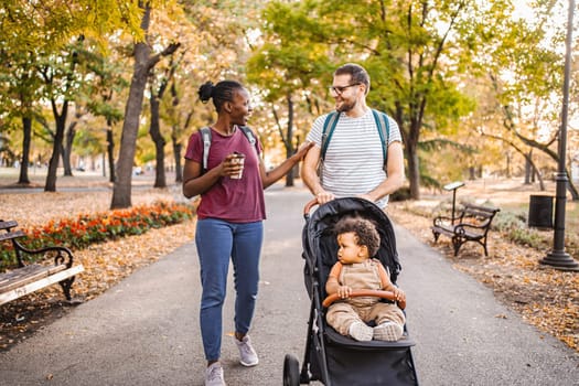 Mixed race couple walks their son's stroller through the park.
