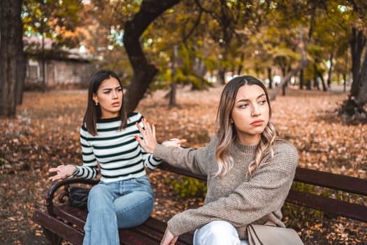 Two women are sitting on a park bench and are signaling to each other