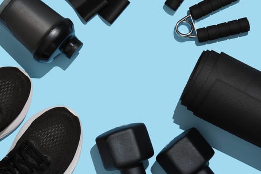 Frame of black exercise equipment for working out at home on blue background. Fitness, sports items, healthy lifestyle concept. Place for your text