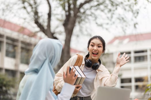 A diverse female student with headphones joyfully waving at her friend while holding books on a university campus, showcasing friendship and enthusiasm for learning.