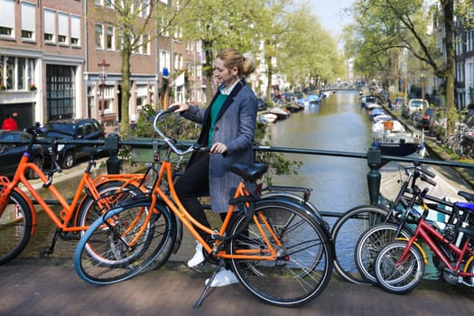 Beautiful blonde woman near the bicycle on the bridge over the water channel in Amsterdam city