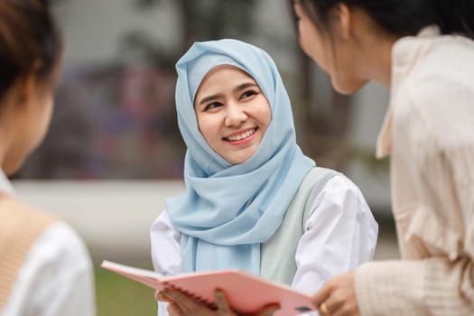 A smiling Muslim woman wearing a hijab engaged in a joyful conversation with her friends outdoors in a university setting.