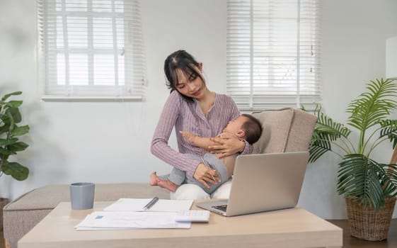 A multitasking mother talking on the phone while gently holding her baby in a comfortable home office environment.