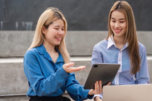Two diverse women working together on a tablet, sharing ideas and collaborating in a contemporary outdoor environment.