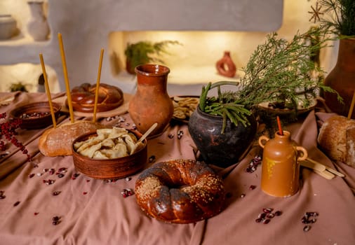 traditional table for a holiday. on the table close-up round bread, loaf, plate with dumplings, clay pot with ears of corn and pine branches. in the background wall with backlight