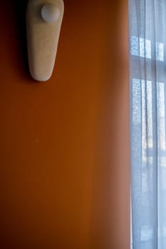 a wall of rich beige color with a lamp. next to a large window. the lamp is oval, it hangs on the wall with ceramic elements.