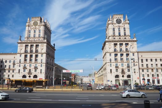 Minsk, Belarus, April 10, 2024: Station Square in front of the railway station. Cars, trucks and buses pass by. People are walking. Sunny spring day. Majestic tower buildings and Kirov Avenue.