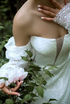 close-up of bride's details white dress and open shoulders. among flowering trees. girl's hand close-up with manicure. she stands among pink cherry blossoms, white dress with sequins and long sleeves.