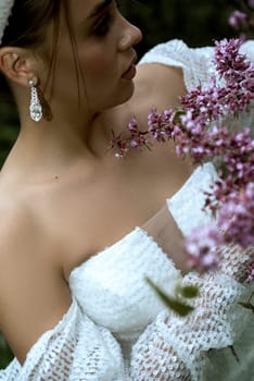 close up of bride details white dress and open shoulders. among blossoming trees. brunette girl, hair in a bun. she stands among blossoming sakura pink, white dress with sequins and long sleeves.