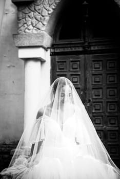 bride in a white dress with open shoulders, with a veil, a bouquet of lilies of the valley. the brunette has a smooth hairstyle gathered in a bun. the bride is covered with a veil, black white photo