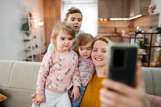 Mother and her three daughters are sitting on the couch and taking a selfie in the living room at home.