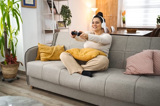 Woman with wireless headphones having fun playing video games at home.