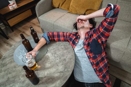 Young man suffering from hangover after night of drinking alcohol at home