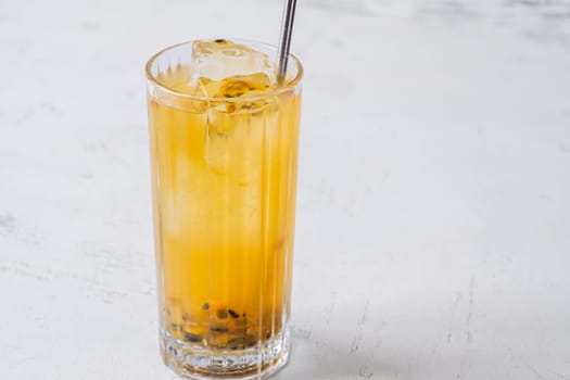 Passion Fruit Caipirinha cocktail in highball glass with straw on white wooden