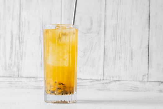 Passion Fruit Caipirinha cocktail in highball glass with straw on white wooden