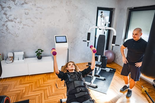 A woman lifts weights while wearing an electrical stimulation device.