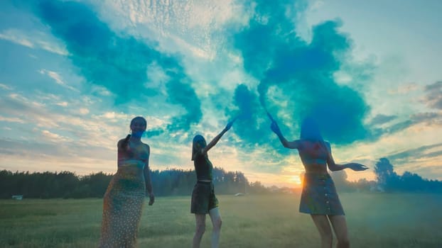 Three school friends enjoying a vibrant celebration, waving colorful smoke bombs against a picturesque sunset in a field