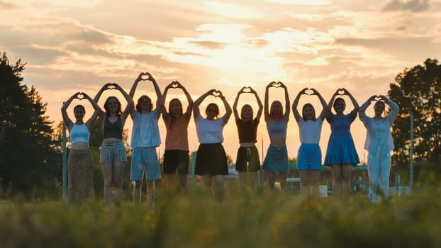 Group of school friends making heart shape with their hands at sunset, symbolizing love, unity, and friendship
