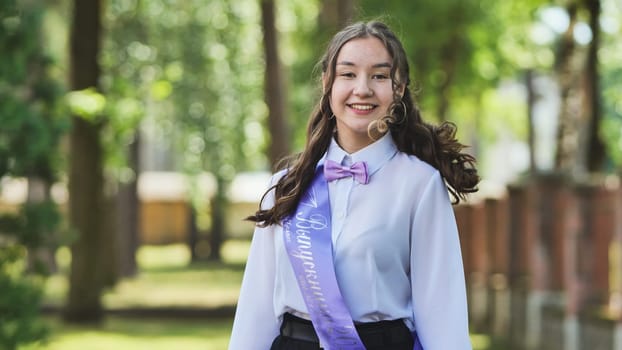 Young woman joyfully marks her final day of school in a park, adorned with a graduation sash and radiating pride and anticipation. Gazing ahead with optimism and assurance for what lies ahead