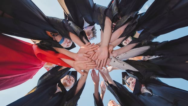 Bottom view of graduated students making a circle with their hands, celebrating their achievement together