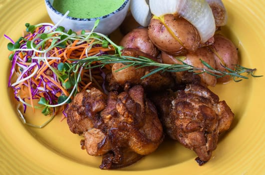 Peruvian Chicken with Green Sauce and salad with potato on yellow plate close up side view
