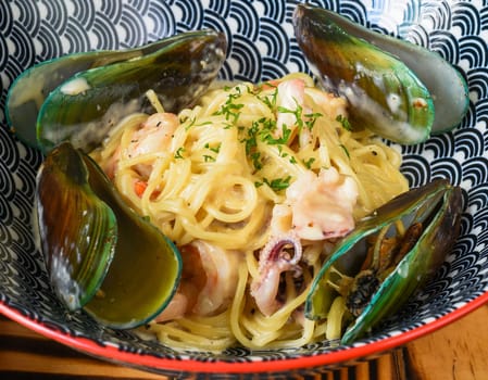 Pasta carbonara with sea food on blue plate isolated on black background side view