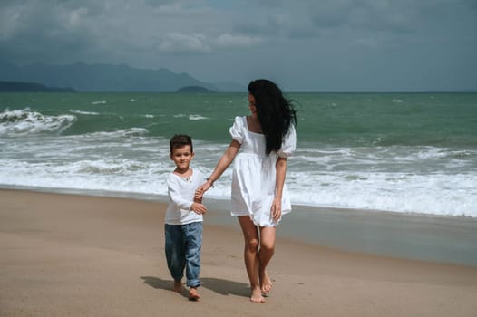Happy mom and son walking along the beach by the sea on summer vacation