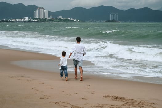 back of dad with a child boy son are walking along the beach by the sea on a summer vacation