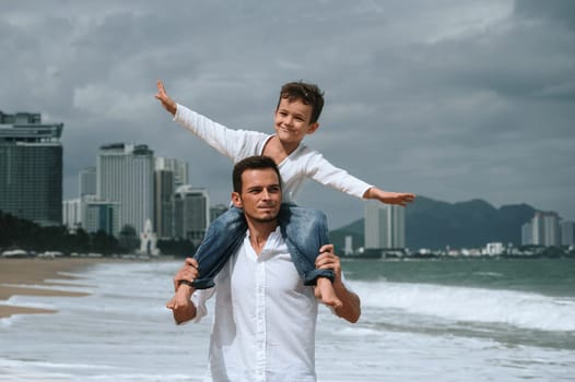 happy father dad with a child boy son on shoulders walking along the beach by the sea in summer on vacation