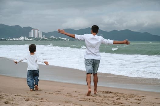 back of happy father dad with a child son are walking along the beach by the sea on a summer vacation