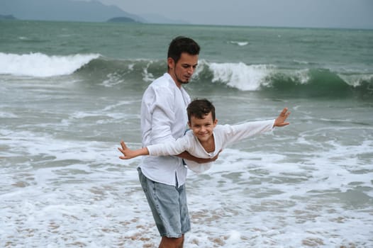 happy father dad with child boy son playing on the beach by the sea in summer on vacation