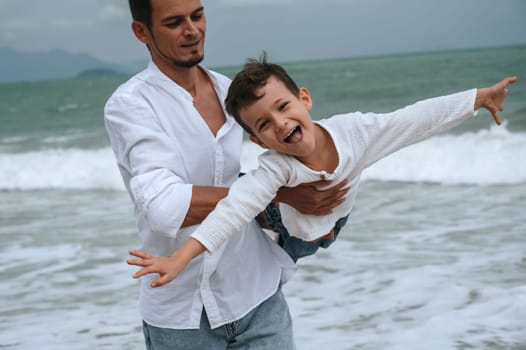 happy dad with child son playing on the beach by the sea in summer on vacation