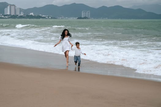 Happy mom and son running along the beach by the sea on summer vacation
