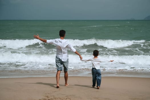back of happy father dad with child boy son running along the beach by the sea in summer on vacation