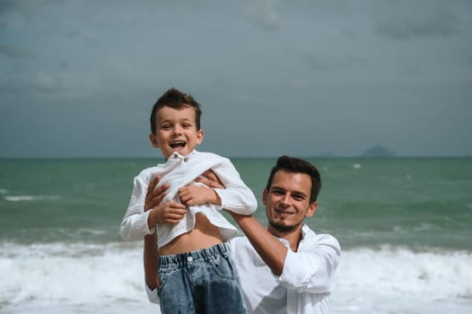 happy father with child boy son playing on the beach by the sea in summer on vacation